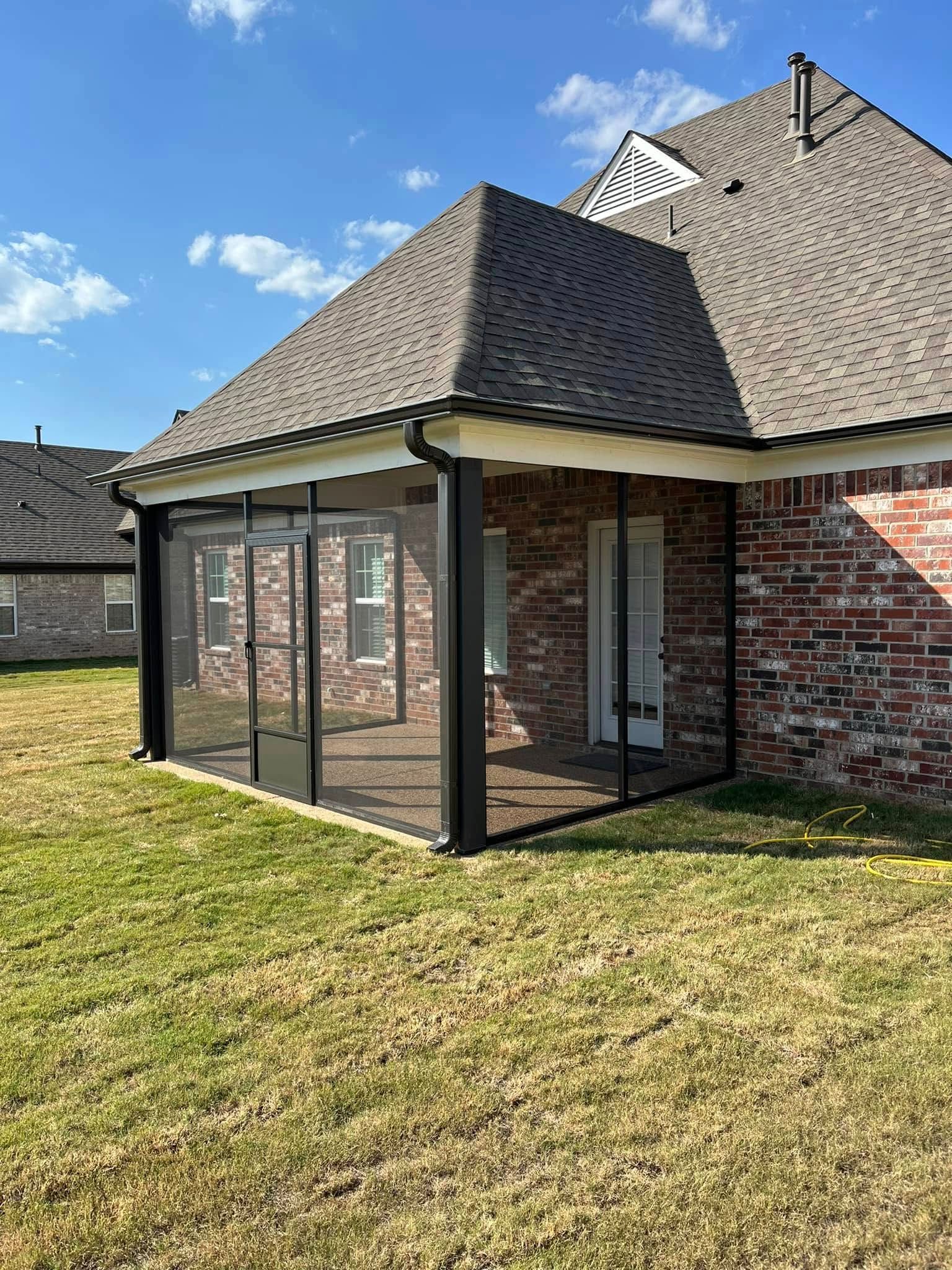 A screened in porch with a brick house in the background.