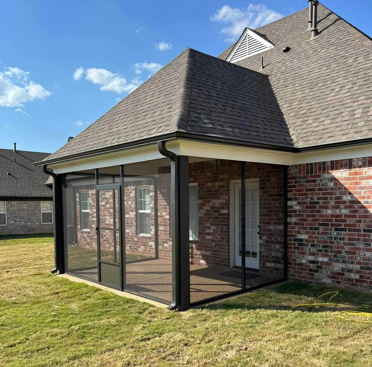 A brick house with a screened in porch and a gray roof.
