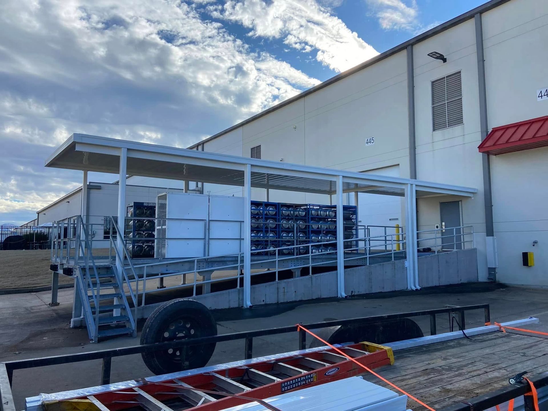 A trailer with a ladder attached to it is parked in front of a building.