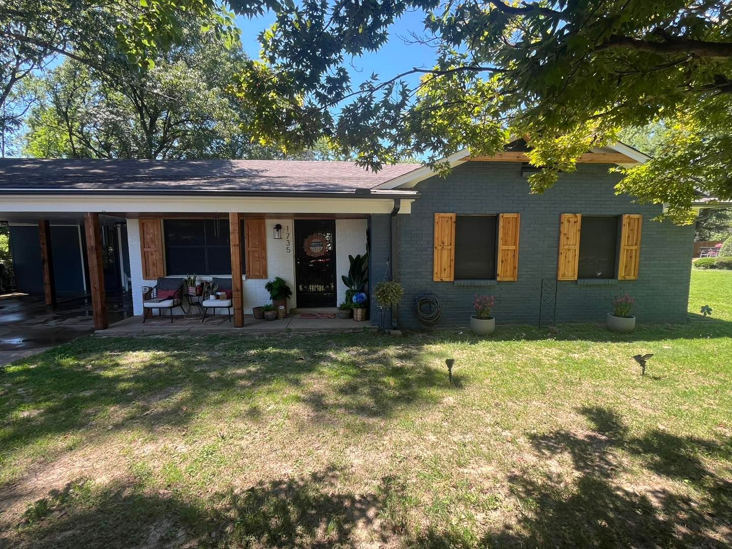 A house with a porch and shutters on the windows is sitting on top of a lush green field.