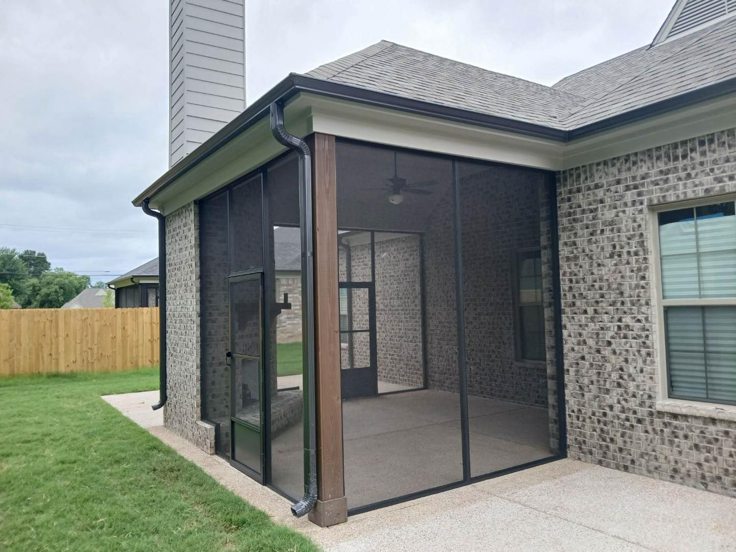 A screened in porch on the side of a brick house.
