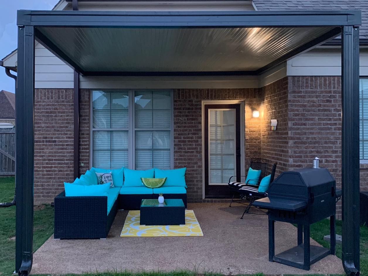 A patio with a couch , table , chairs and a grill under a pergola.