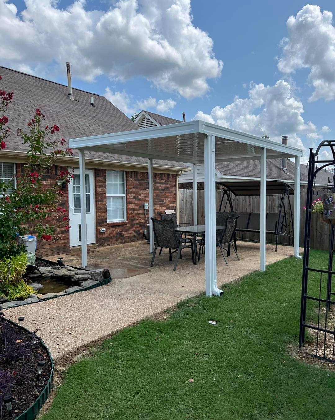 A patio with a table and chairs under a pergola in the backyard of a house.