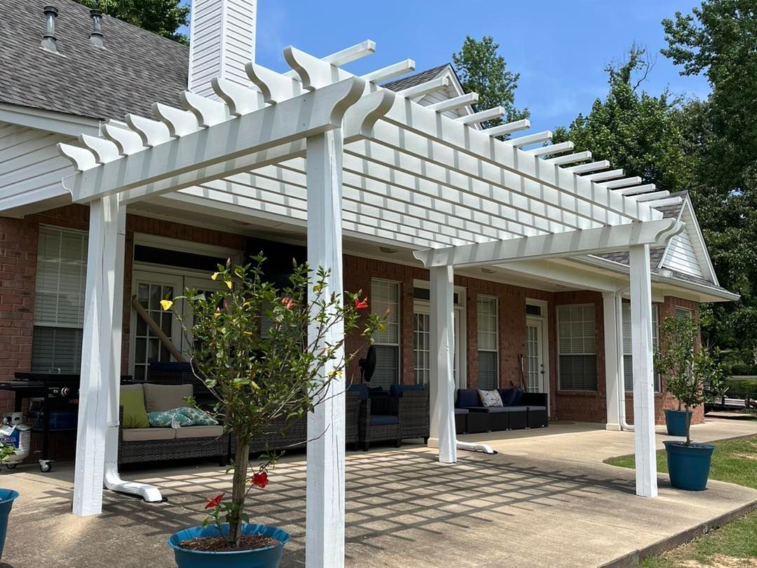 A white pergola is sitting on top of a patio next to a house.