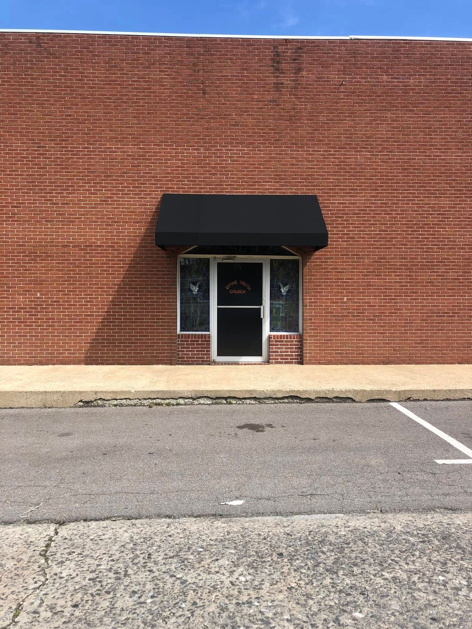 A brick building with a black awning over the door and a parking lot in front of it.