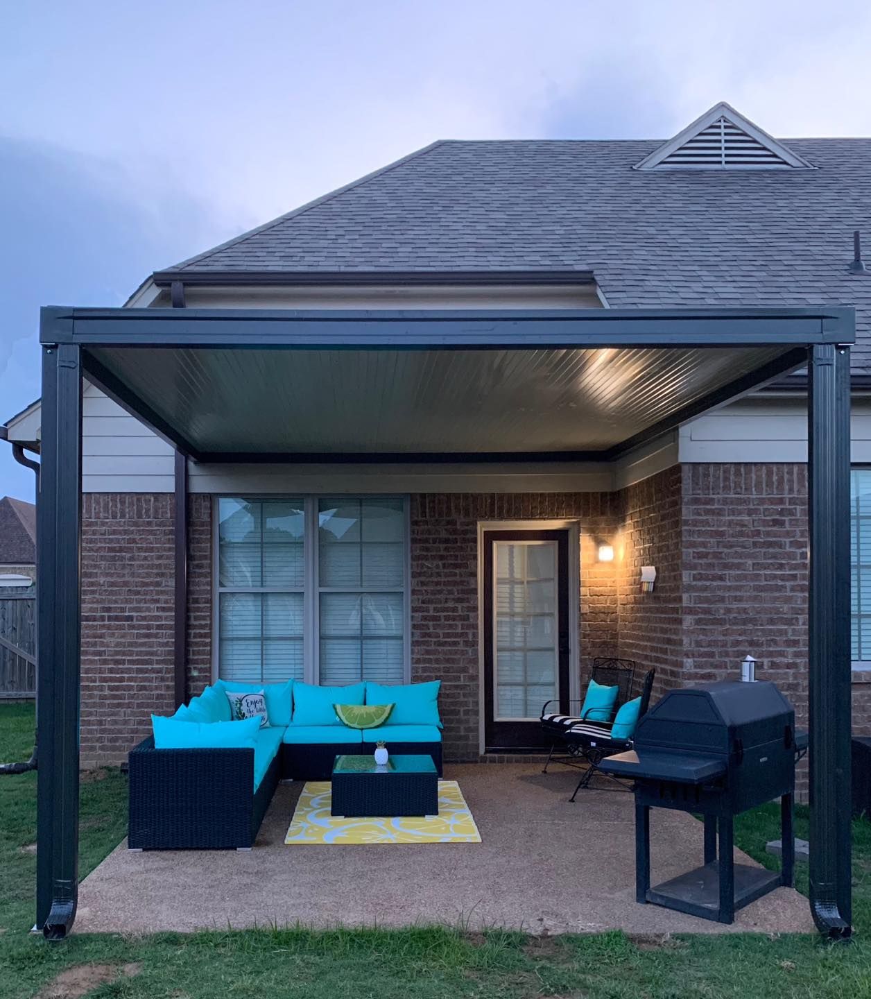A patio with a pergola and a couch in front of a brick house.