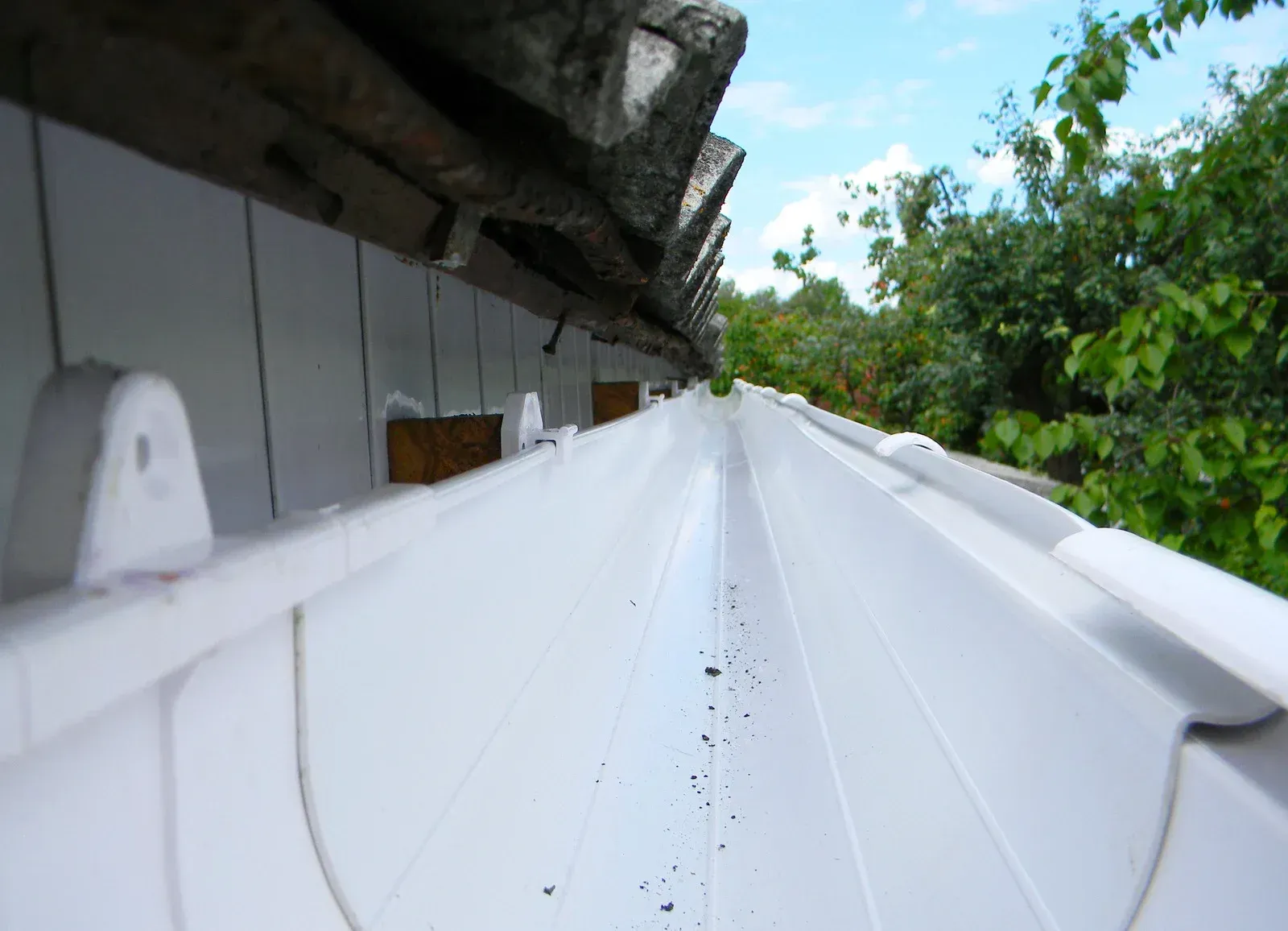A white gutter on a roof with trees in the background