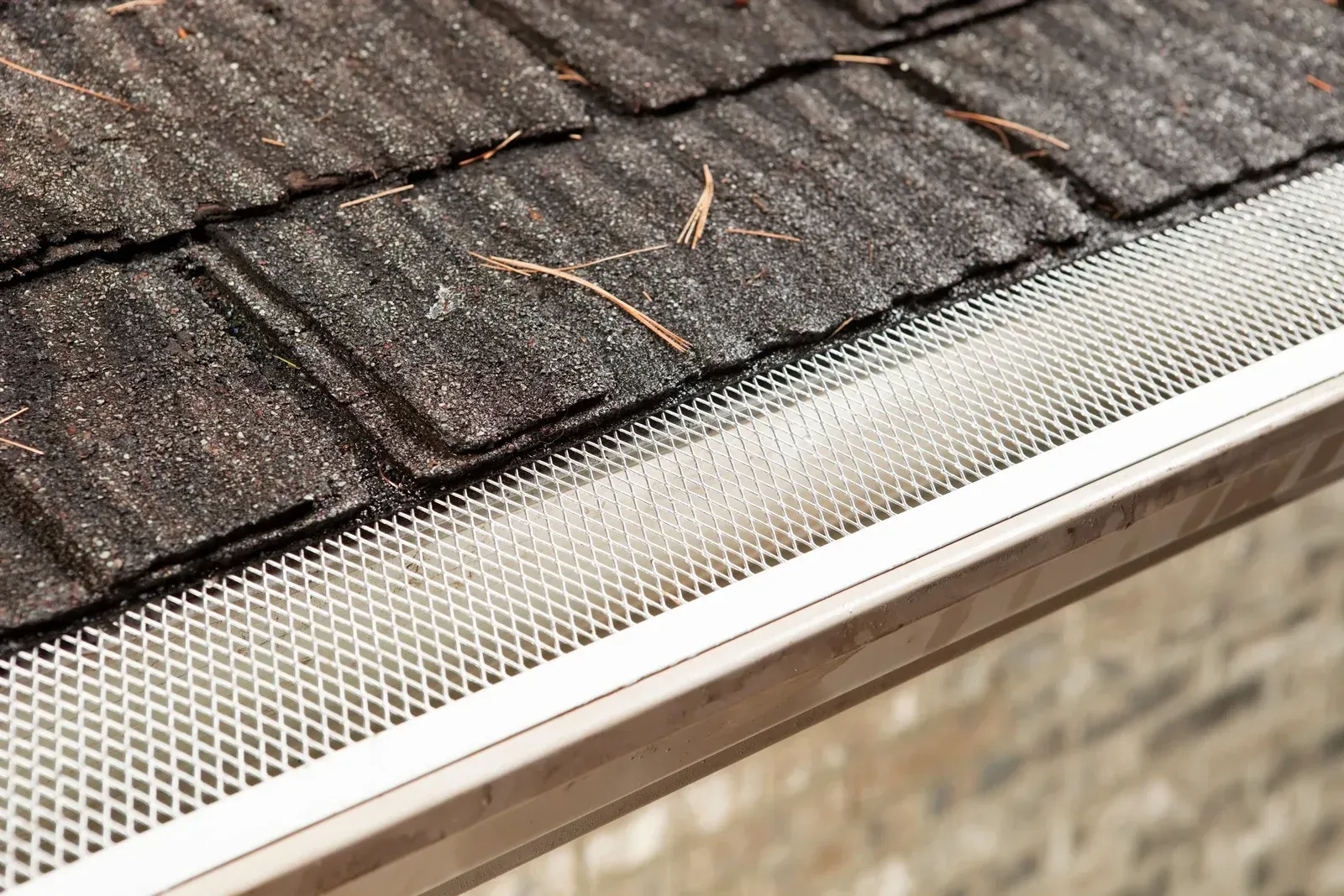 A close up of a gutter on a roof with shingles.