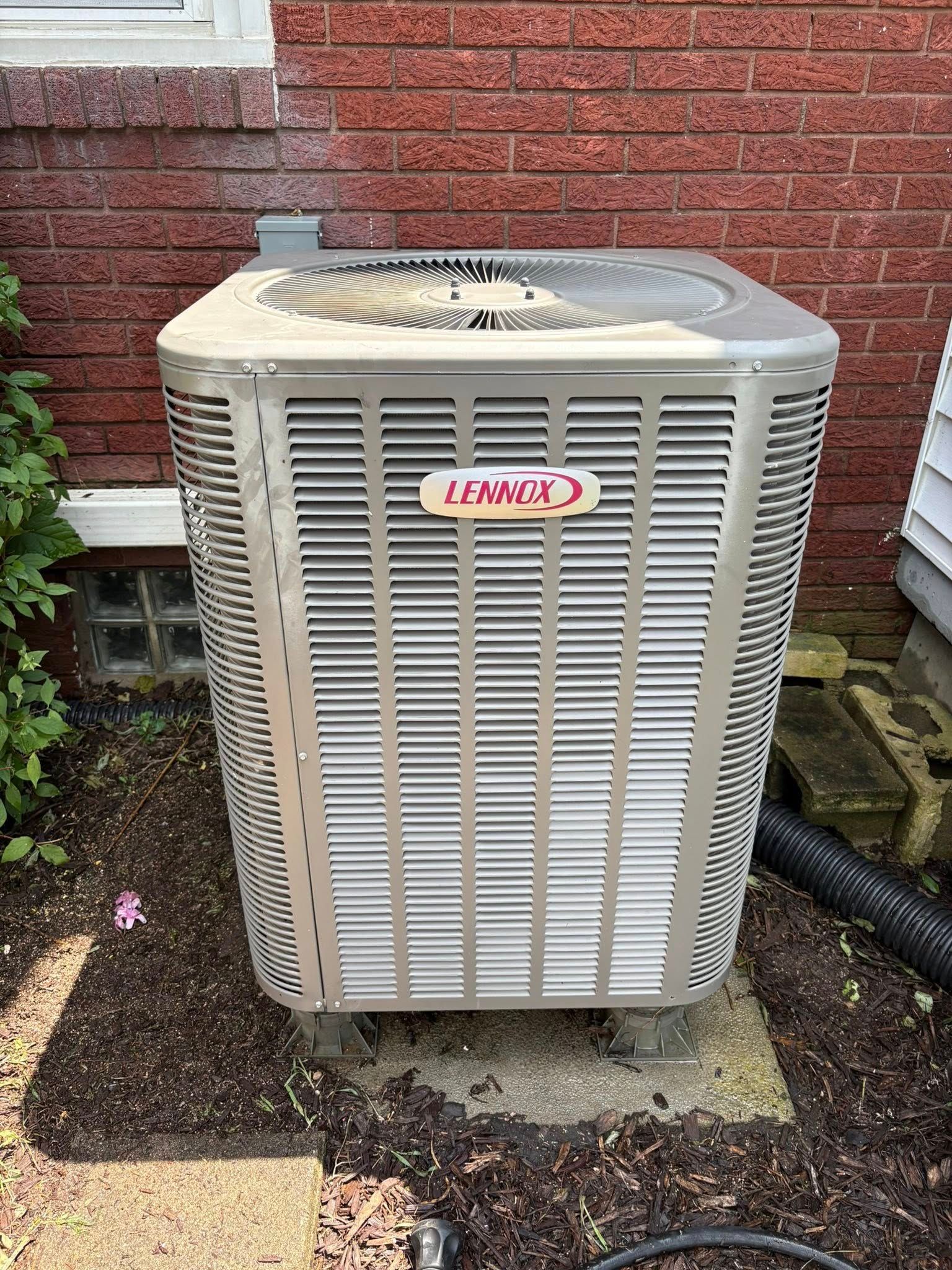 Lennox air conditioning unit outside against a brick wall.