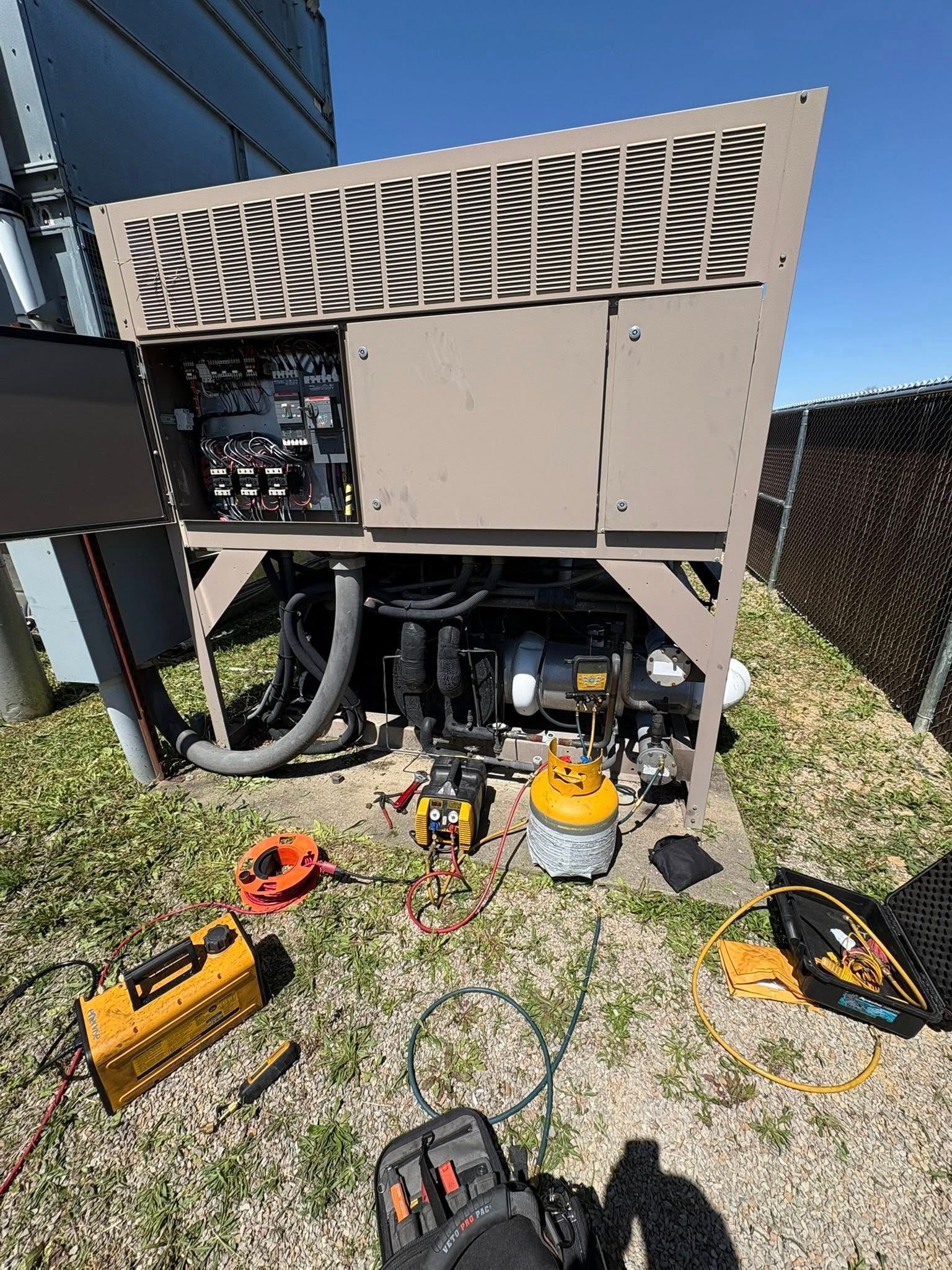HVAC unit with open panels outdoors on a sunny day, surrounded by tools and electrical equipment.