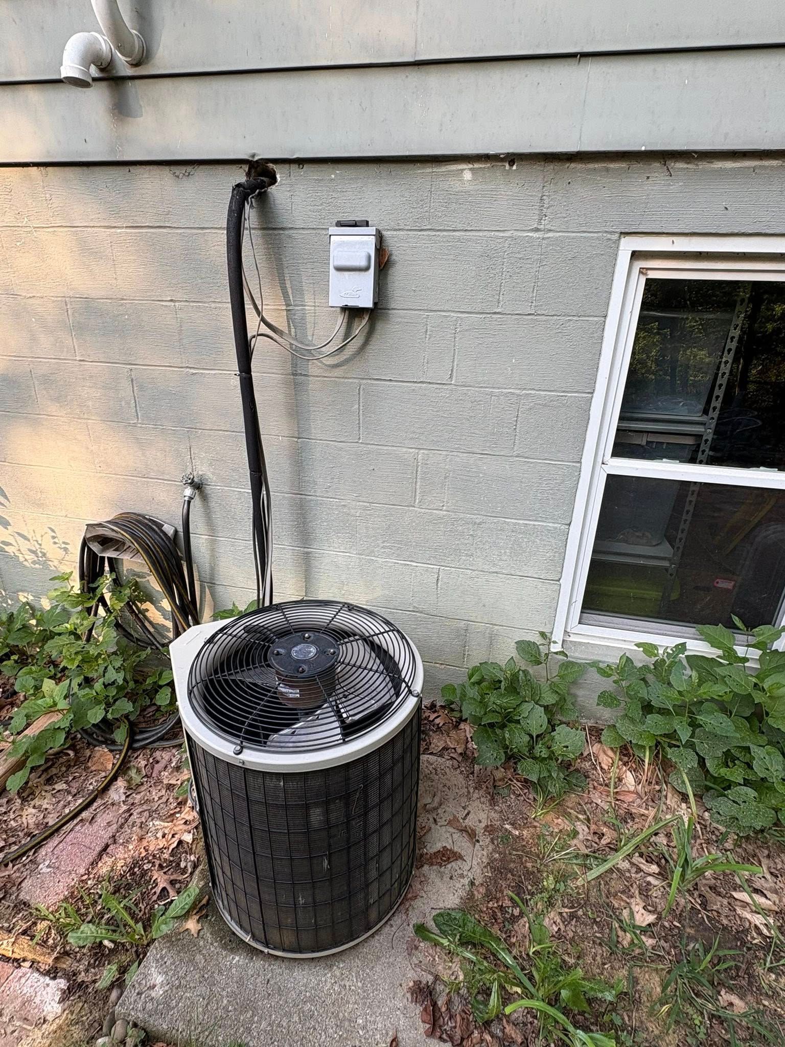 Air conditioning unit next to a house wall, electrical box, and window.