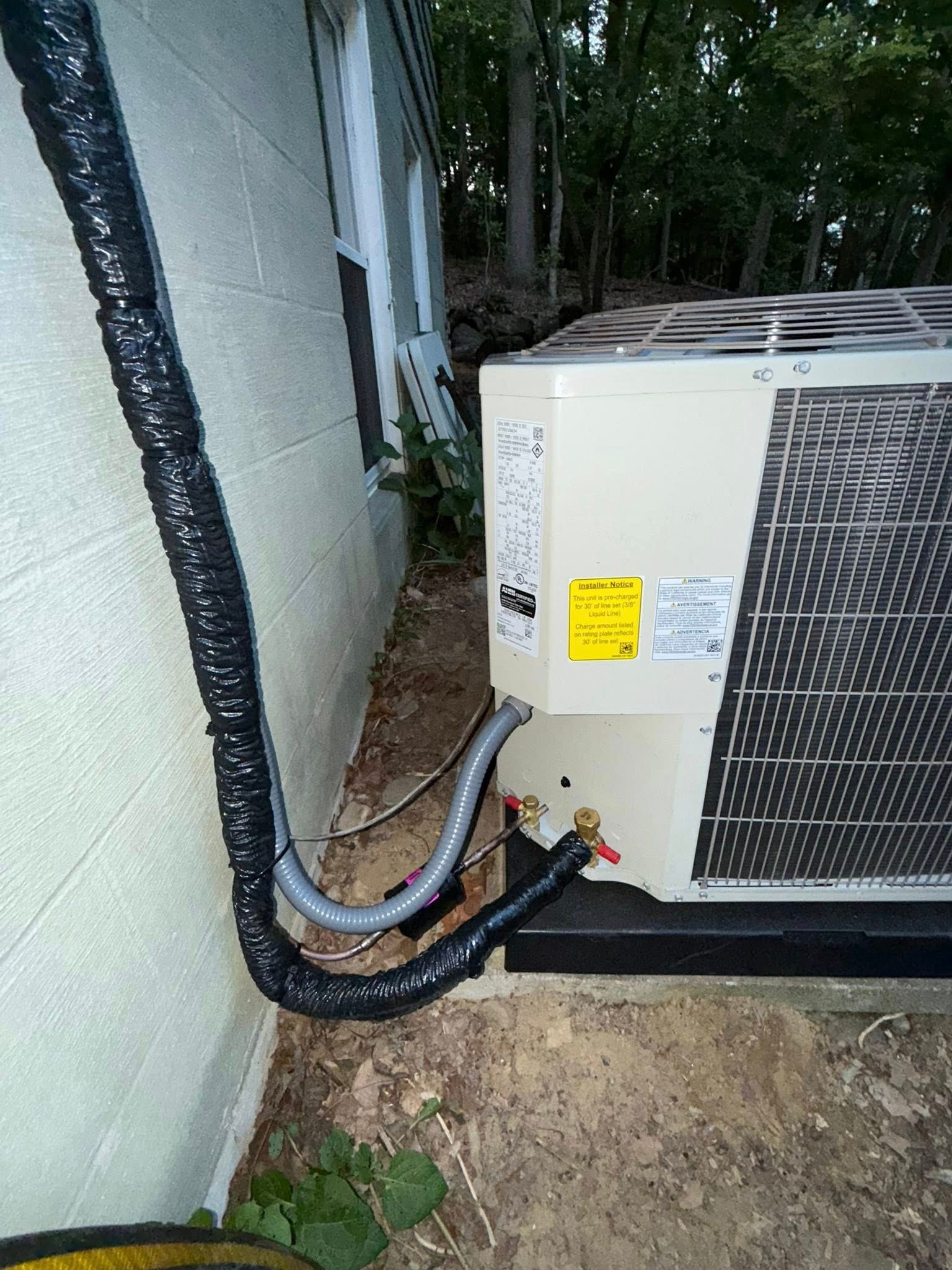 AC unit with black insulated tubing against a light-colored building.
