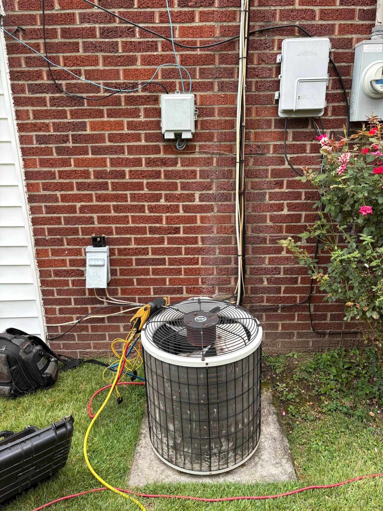 AC unit on a concrete pad near a brick wall, connected by wires.
