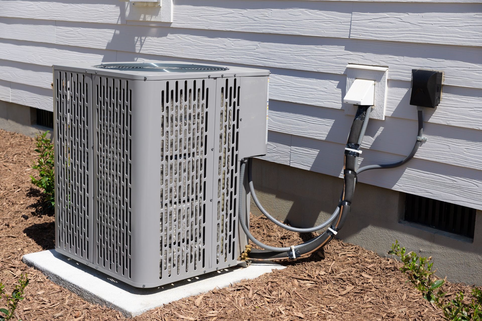 Air conditioner unit outside a house on a concrete pad surrounded by mulch.