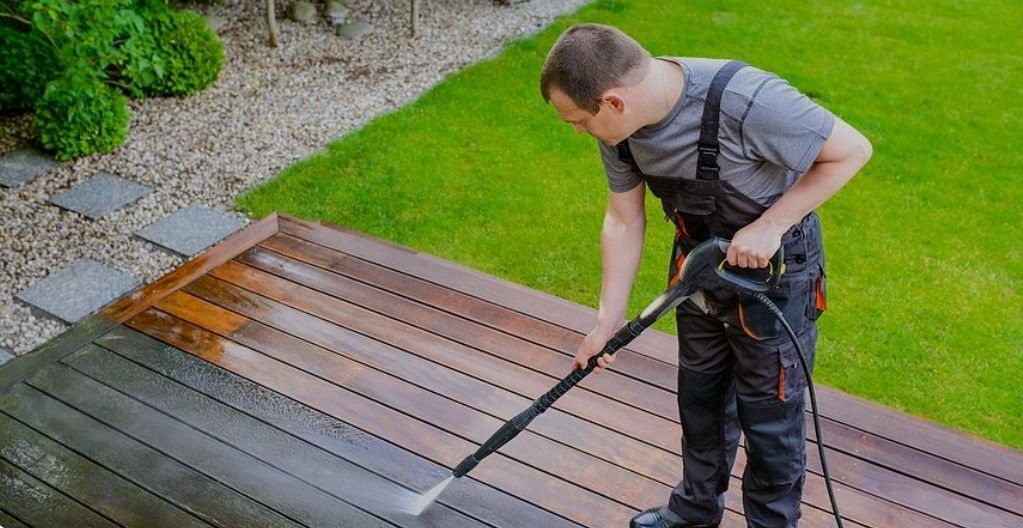 A man is cleaning a wooden deck with a high pressure washer.