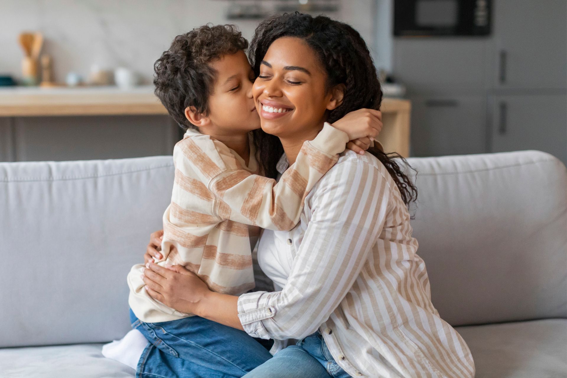 A little boy is kissing his mother on the cheek while sitting on a couch