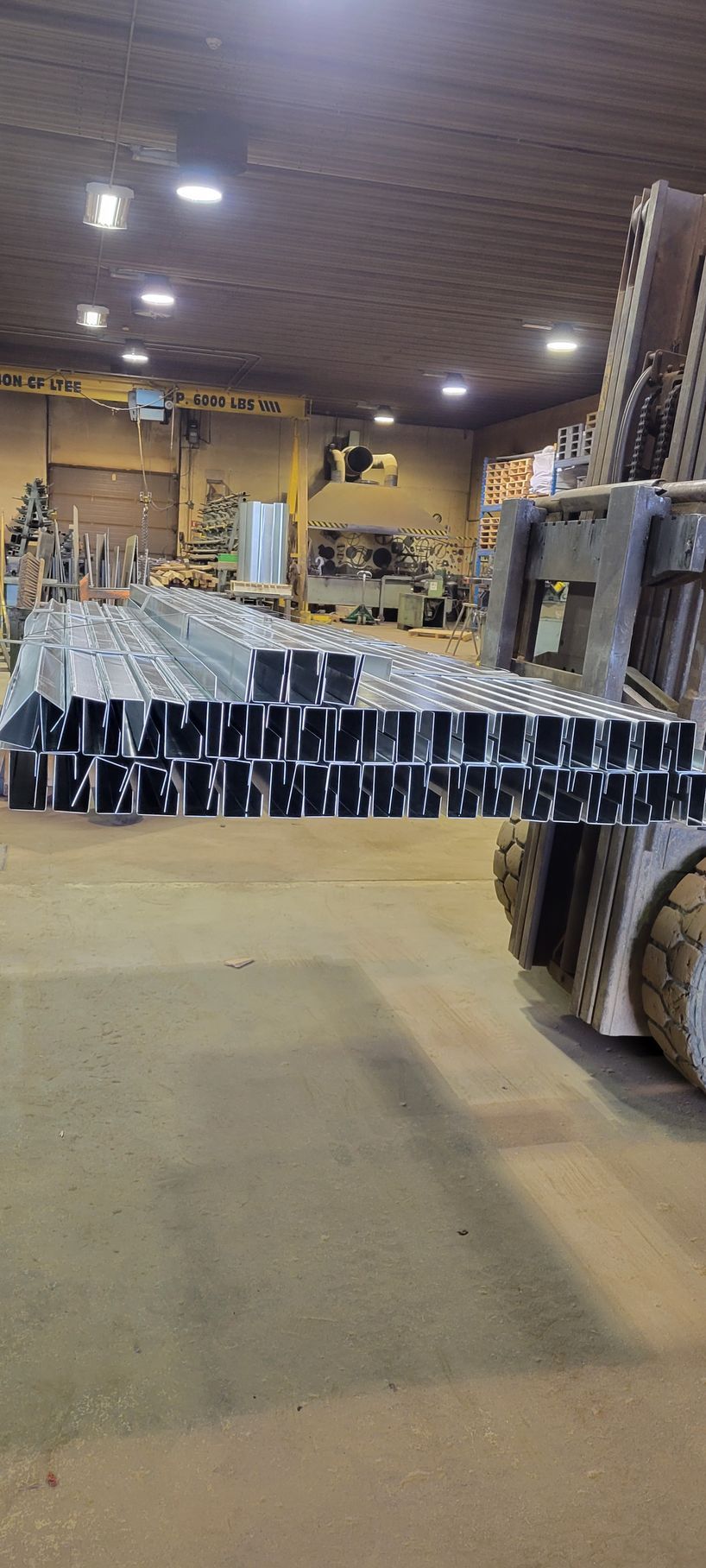 Un chariot élévateur déplace une grande pile de métal dans un entrepôt.