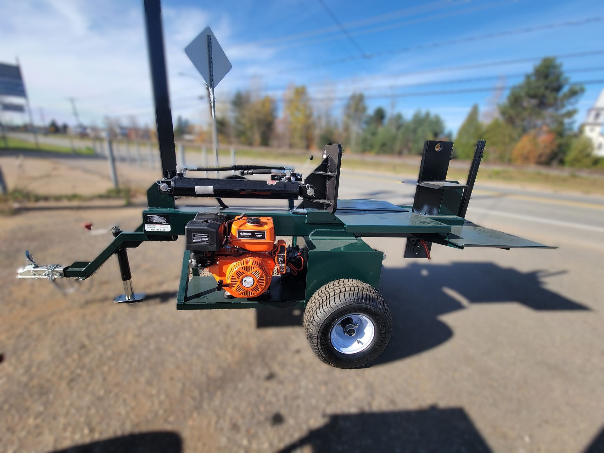 Une fendeuse de bûches sur une remorque est garée sur le bord de la route.