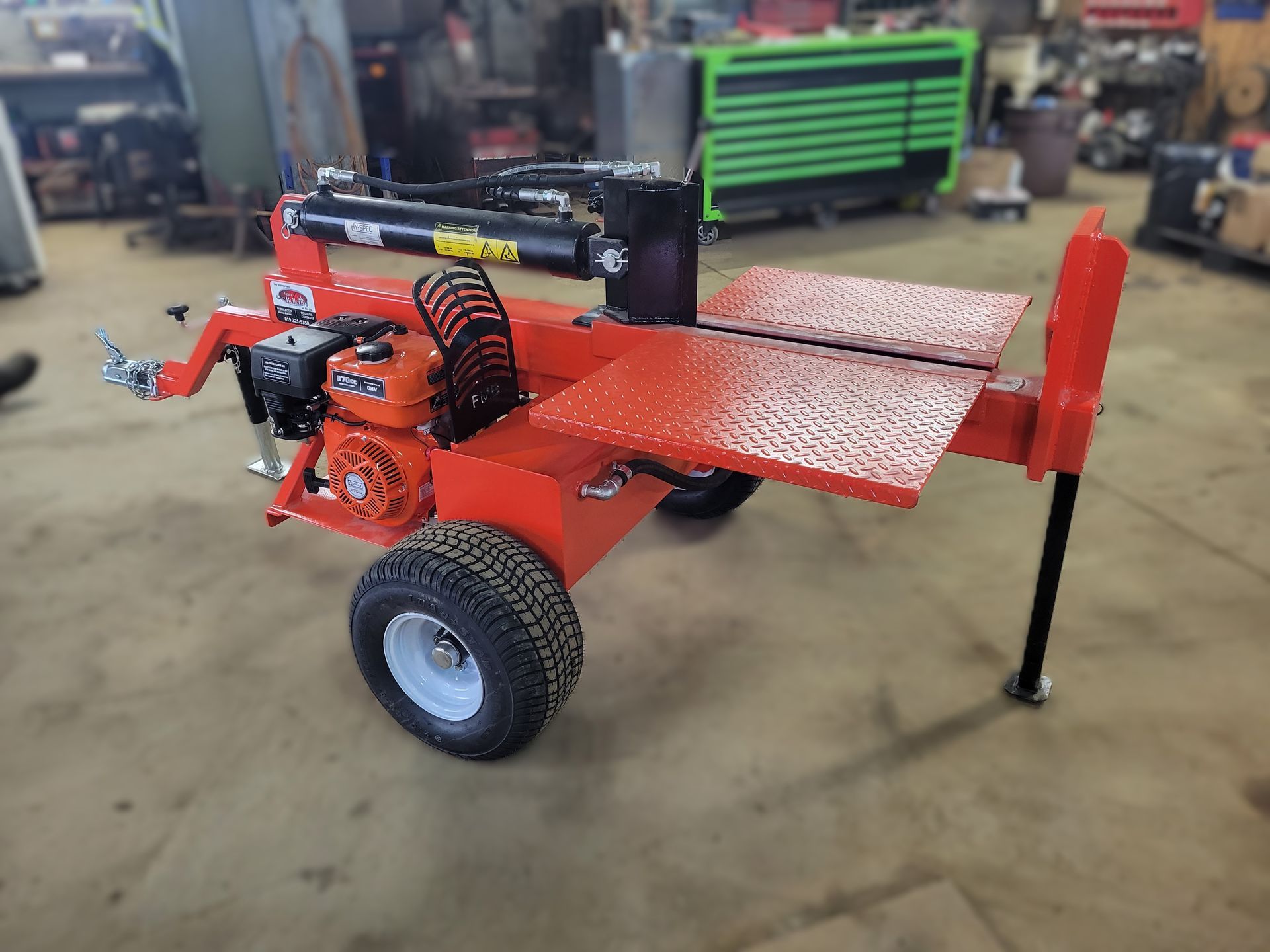 Une fendeuse de bûches rouge est assise sur une remorque dans un garage.