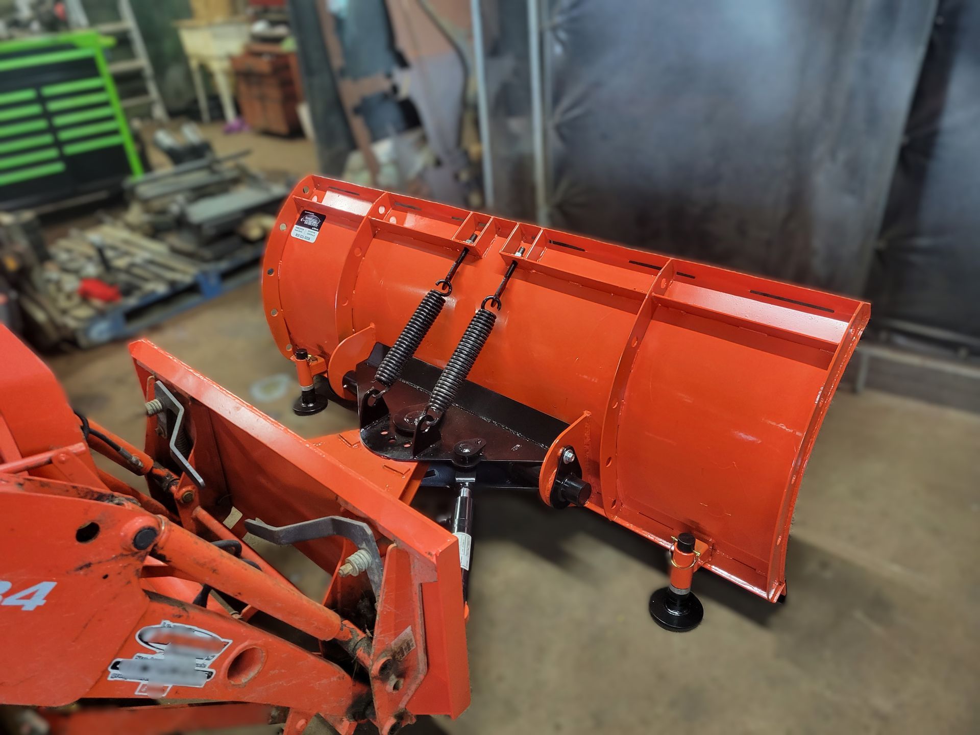 Un chasse-neige orange est assis sur un tracteur dans un garage.