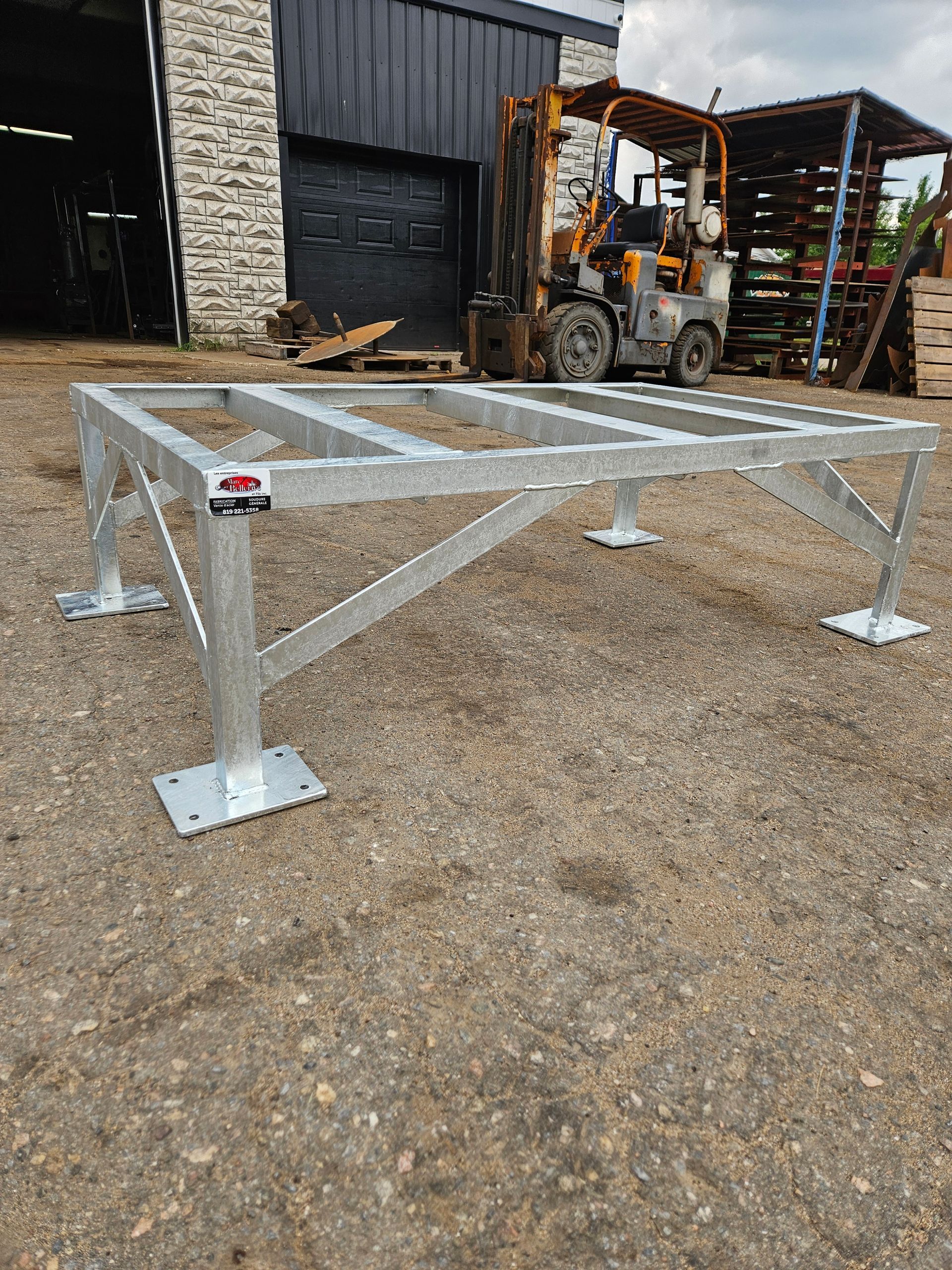 Une structure métallique est posée sur le sol devant un chariot élévateur.