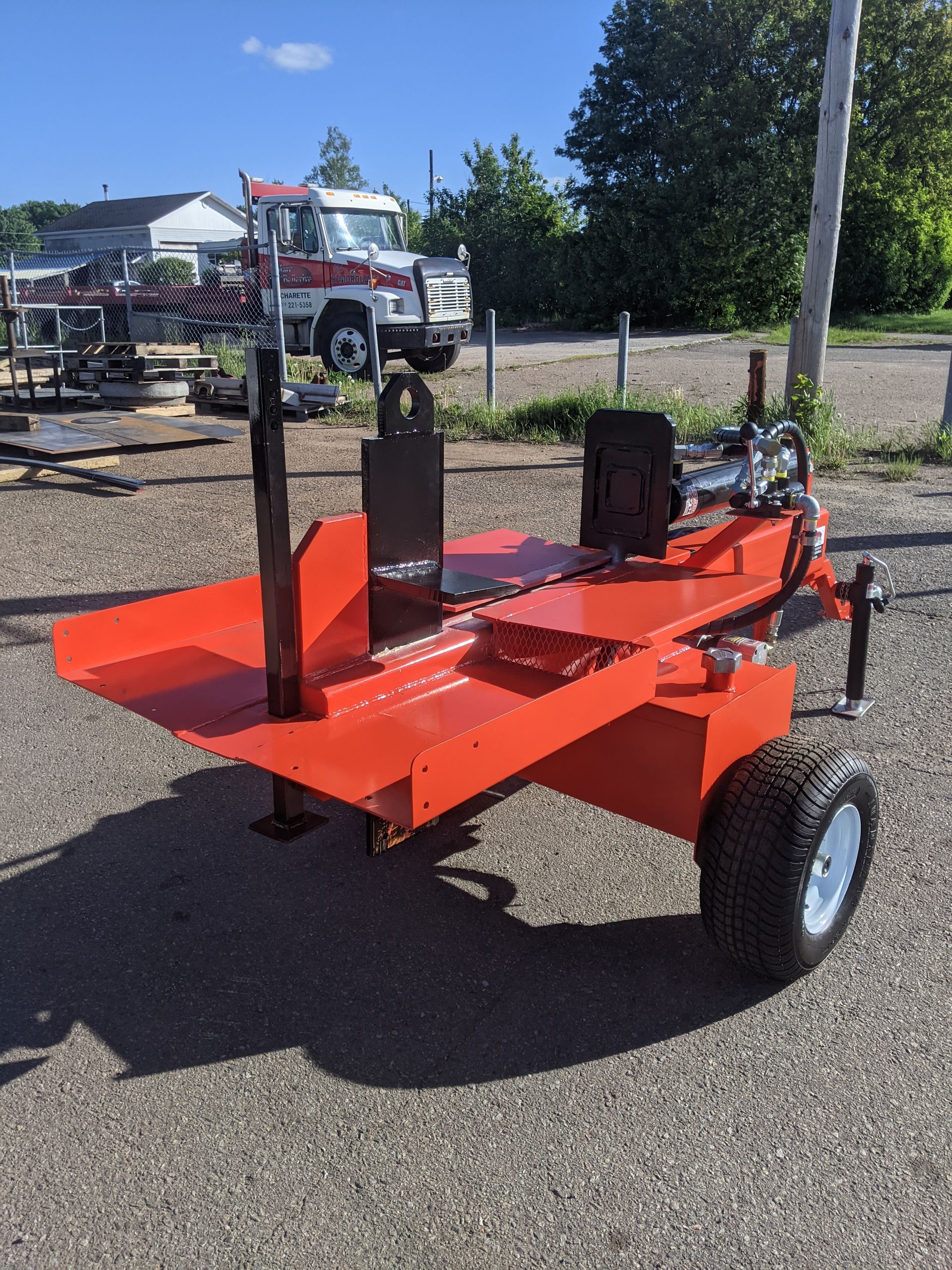Une fendeuse de bûches orange est garée sur le bord de la route.
