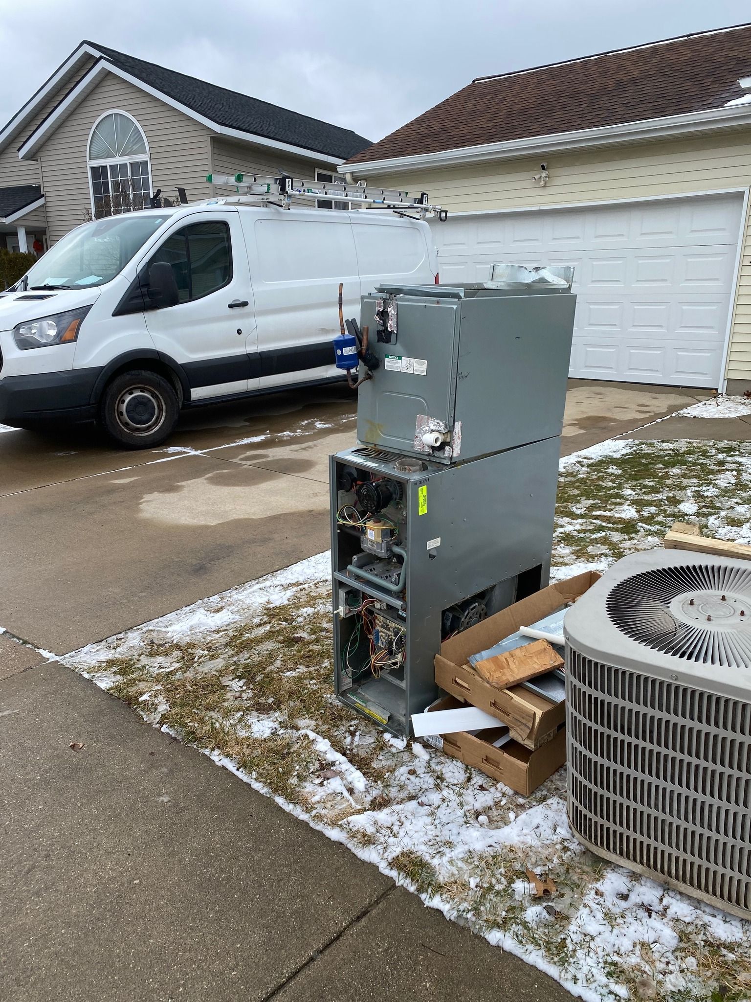 A white service van parked in a driveway next to a discarded HVAC furnace and outdoor air conditioning unit.