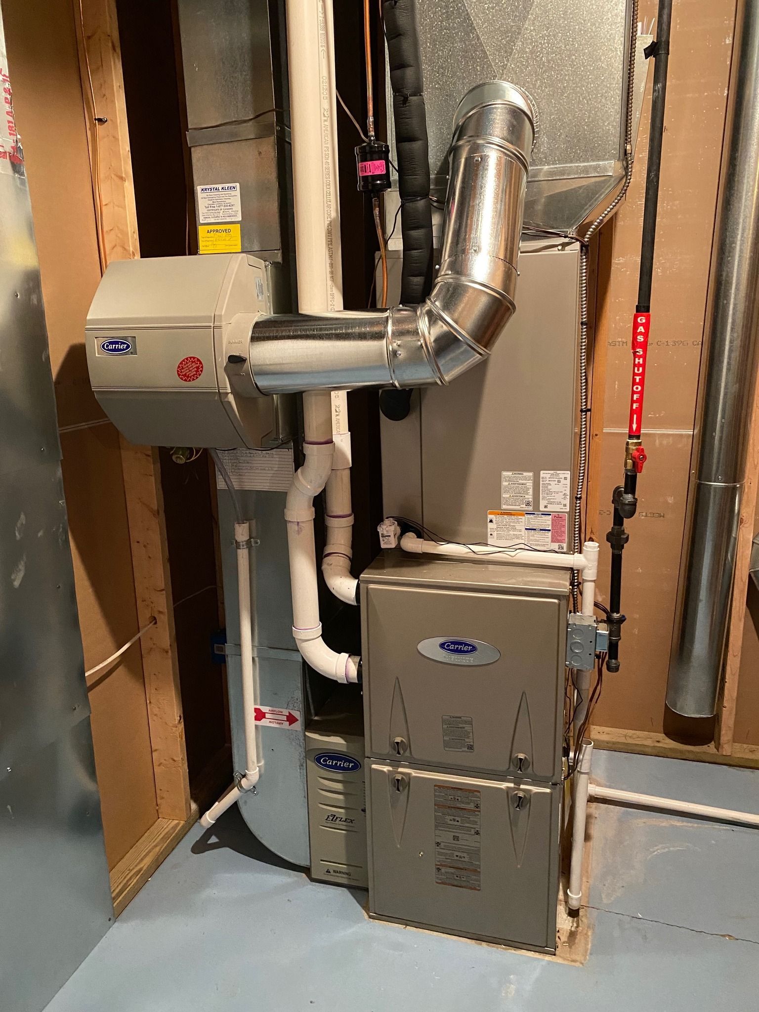 A modern beige HVAC system in a basement featuring a furnace, metal ductwork, and white PVC piping.