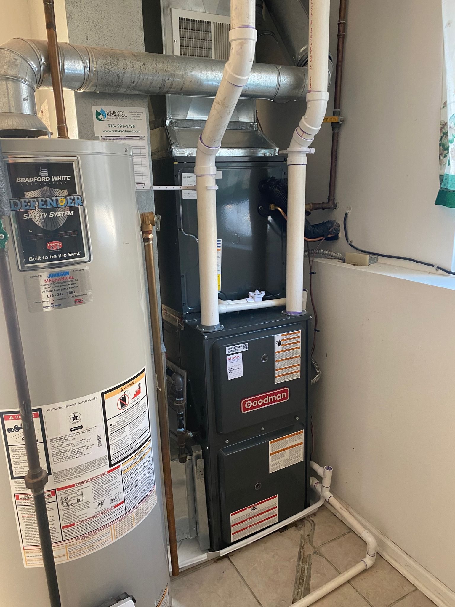 A gas furnace and a water heater stand side-by-side in a utility room with white walls and tiled floors.