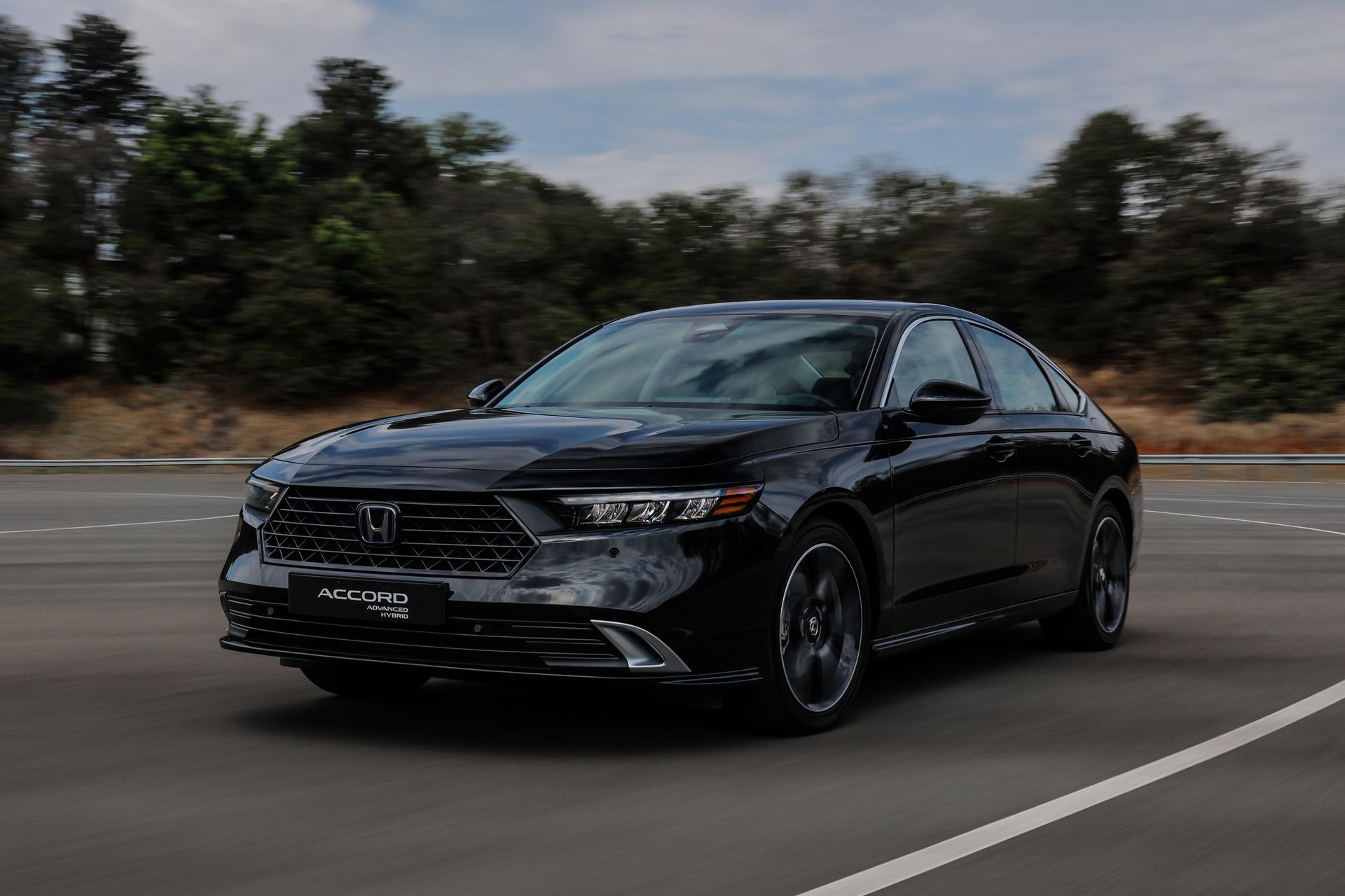 Sedan Honda Accord preto em uma estrada, com árvores ao fundo, durante o dia.
