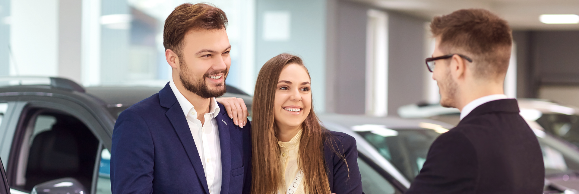 Casal com vendedor em uma concessionária de carros. Sorrindo, conversando sobre detalhes perto de carros estacionados.
