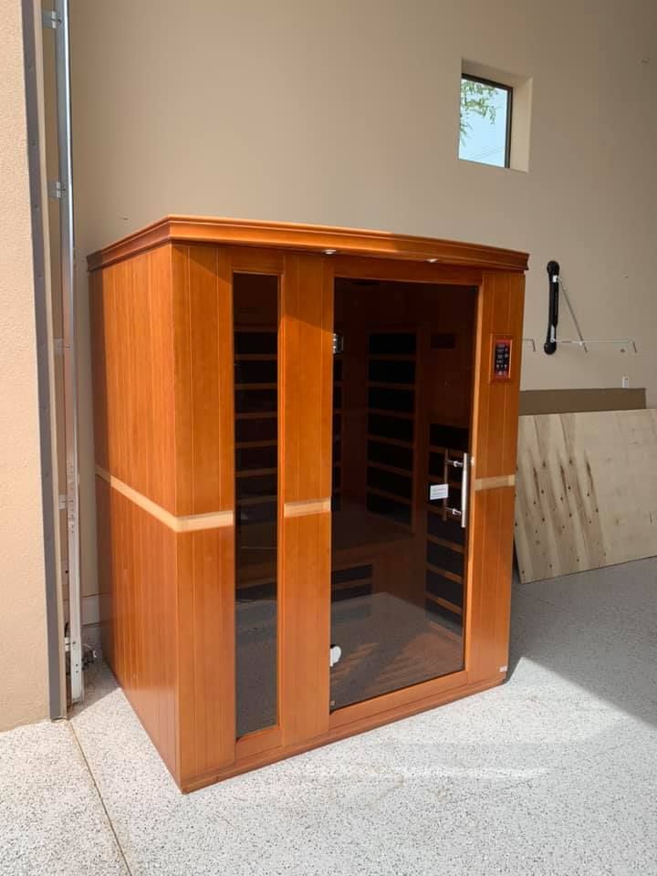 Wooden sauna with glass door and side panels, set against a beige wall in a garage.