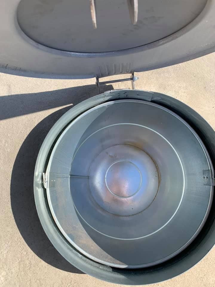 Open metal trash can with lid, set in a circular frame, on a concrete surface.