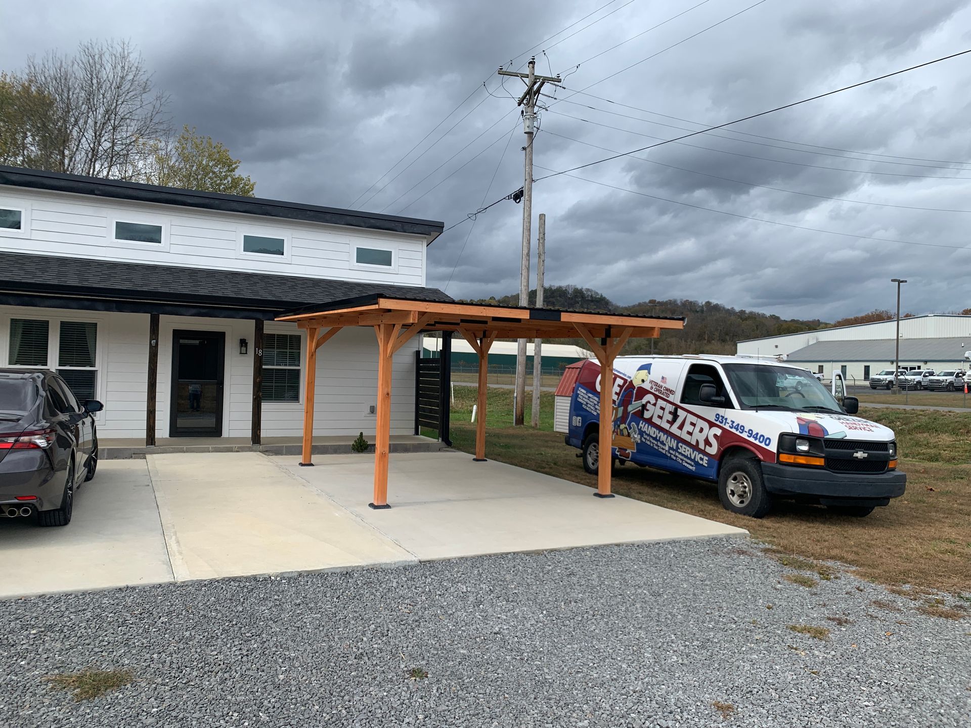 White building with a wooden carport; a van with 