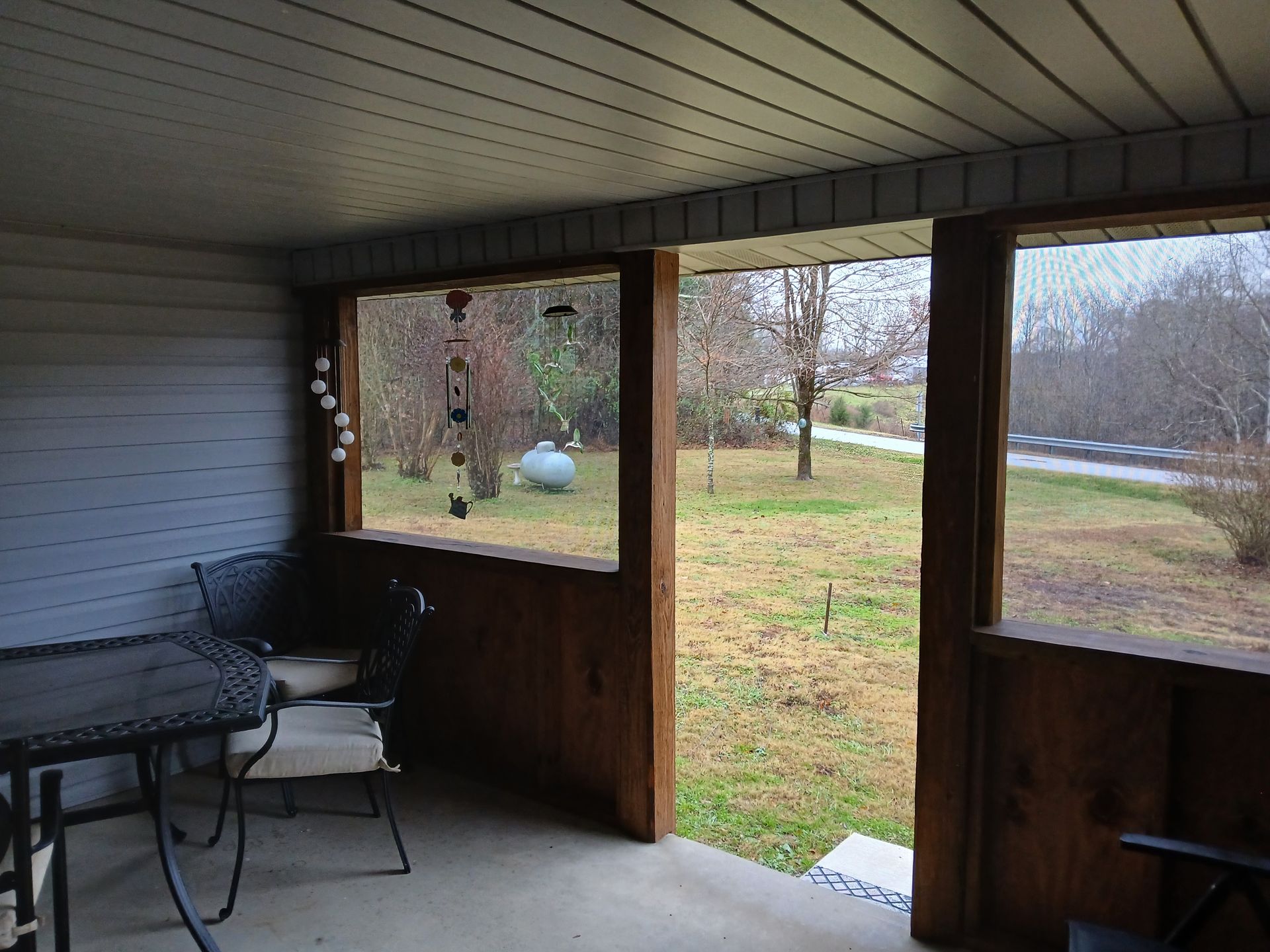 Screened porch with table and chairs overlooking a green yard, overcast day.