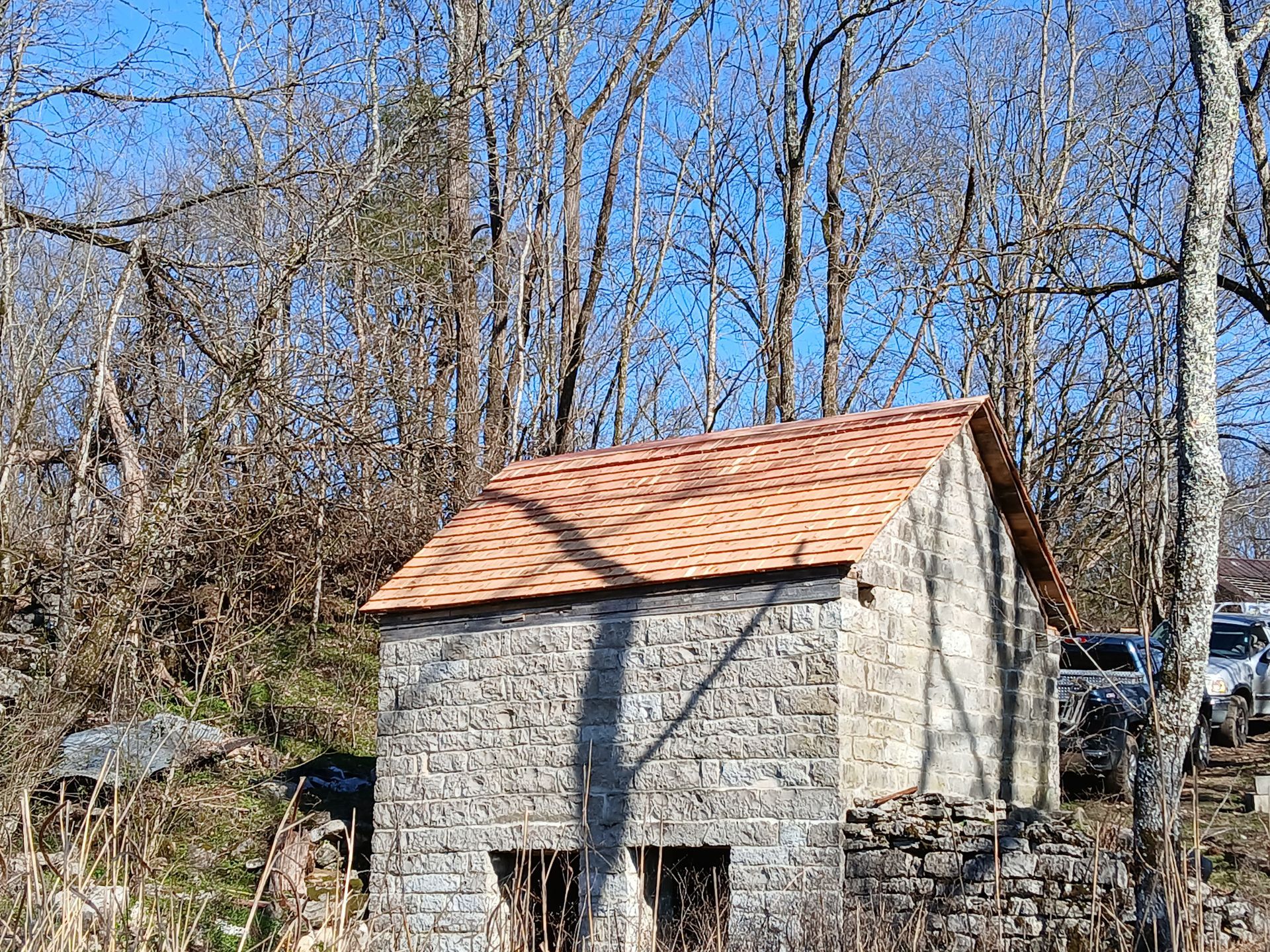 Stone building with red-tiled roof in a wooded area, sunny day.