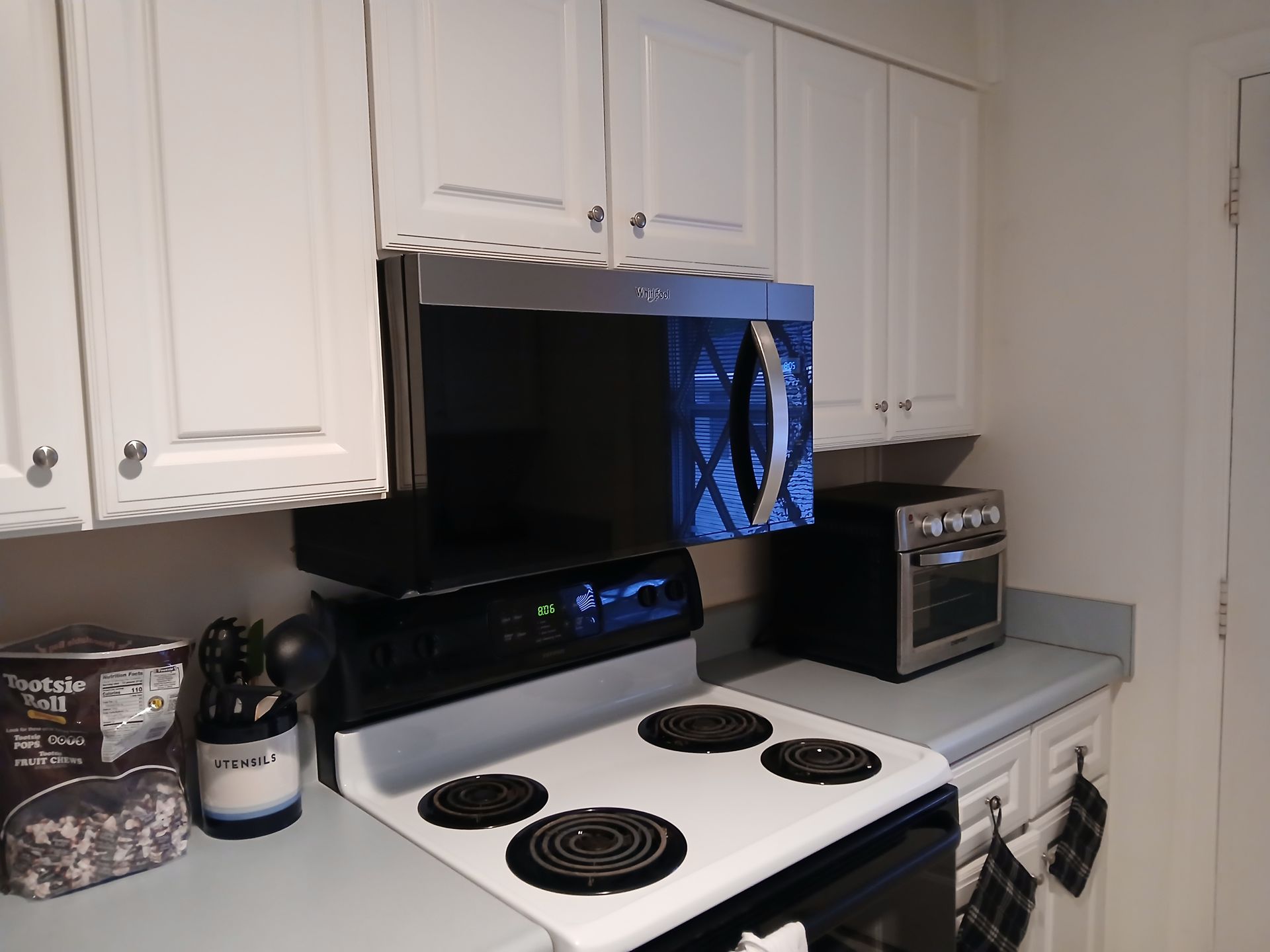 Kitchen with white cabinets, microwave above electric stove, and a countertop oven.