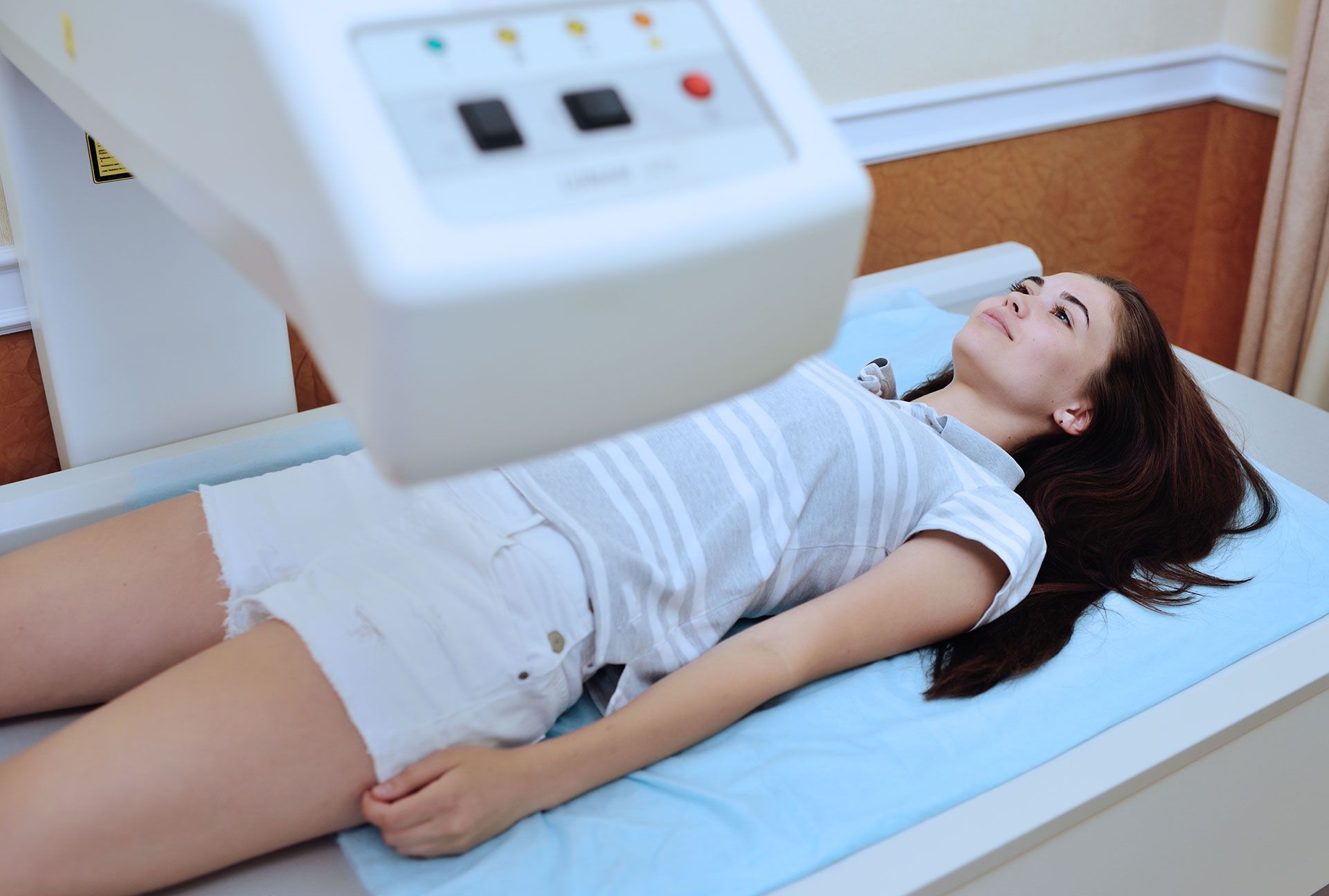 Woman undergoing a bone density scan, lying on a medical bed under a scanning machine.