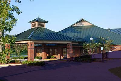 Brick building with green roof, entrance portico, and trees.