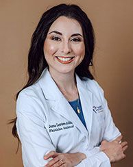 Woman wearing a white lab coat and smiling. The nameplate says 