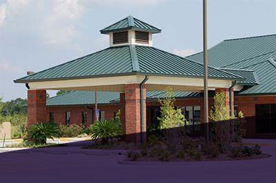 Brick building with green roof, canopy entrance, and flagpole on a sunny day.