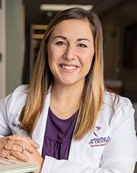 Woman in white coat, smiling, likely a medical professional at a clinic.