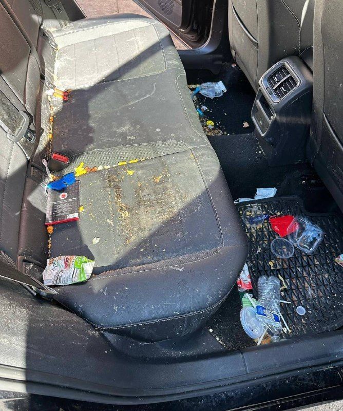 The back seat of a car is covered in trash.