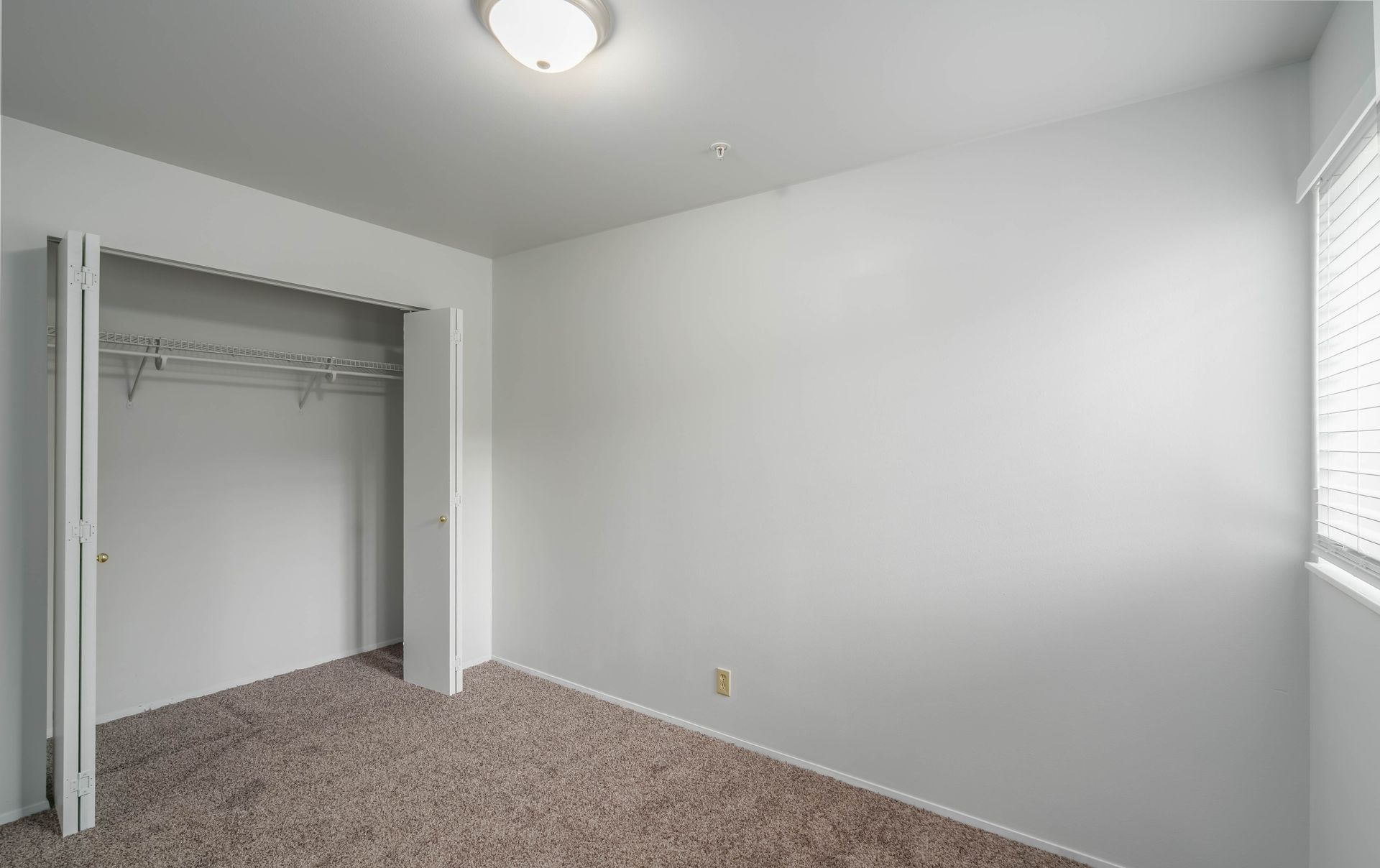 An empty bedroom with a closet and a window.
