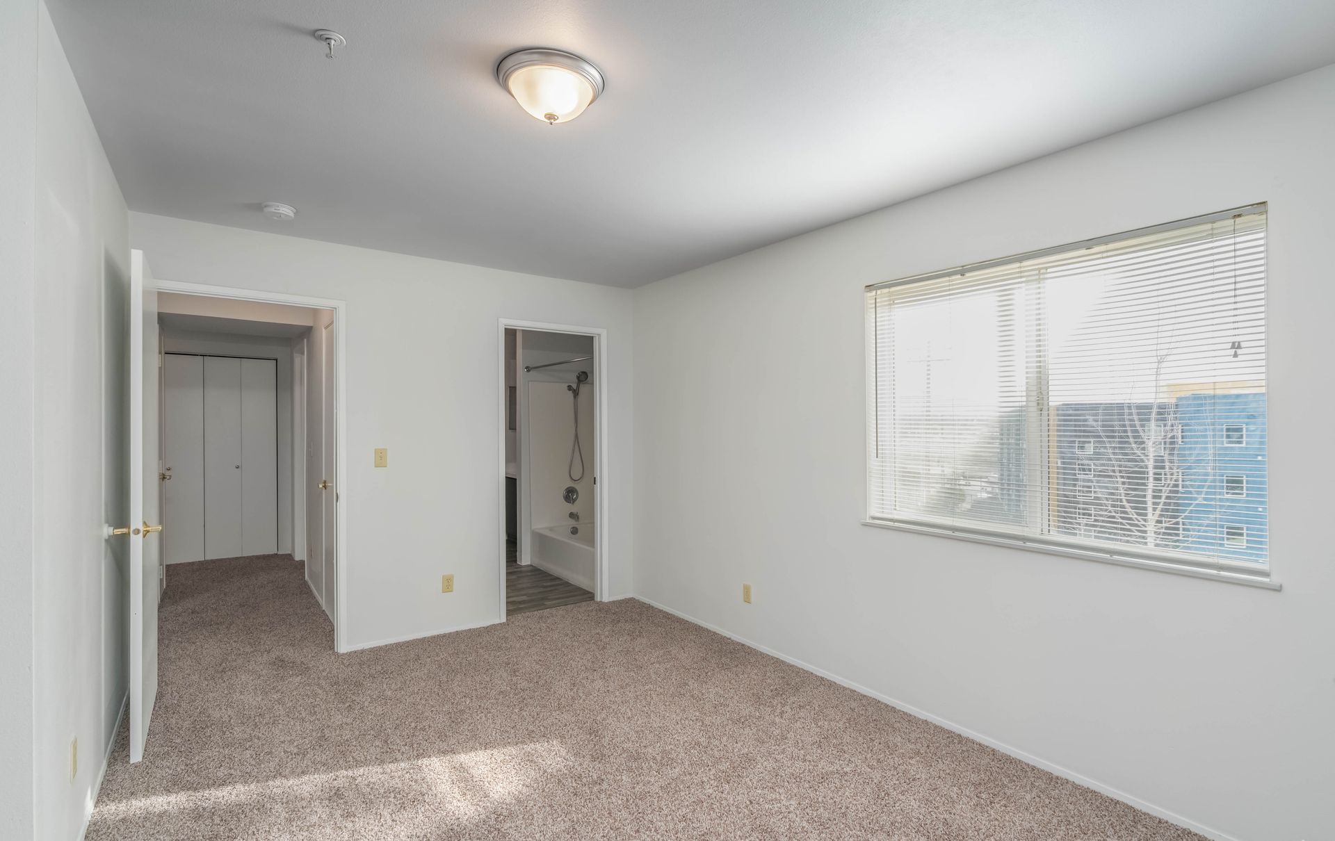 An empty bedroom with a window and a carpeted floor.