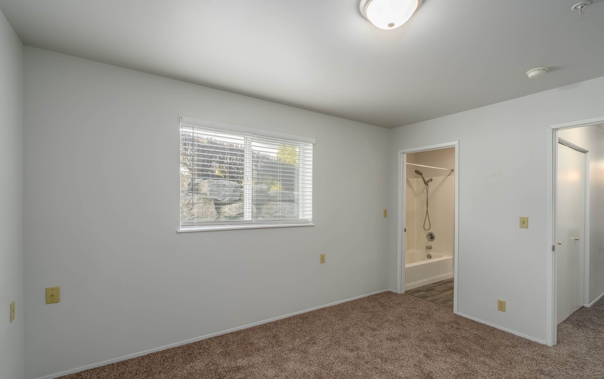 An empty bedroom with a window and a bathroom.