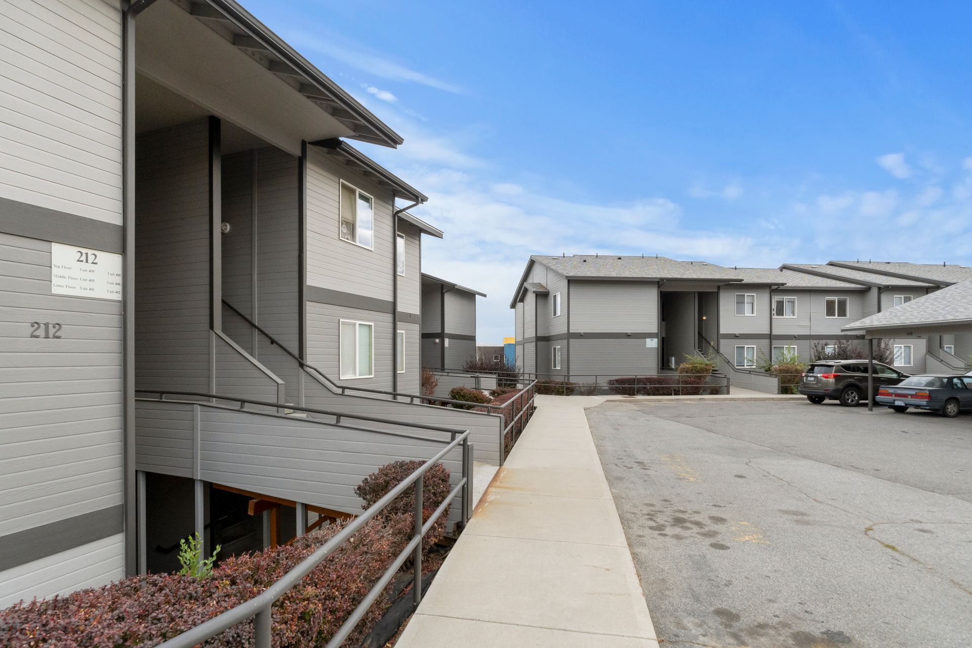 A row of apartment buildings with cars parked in front of them.