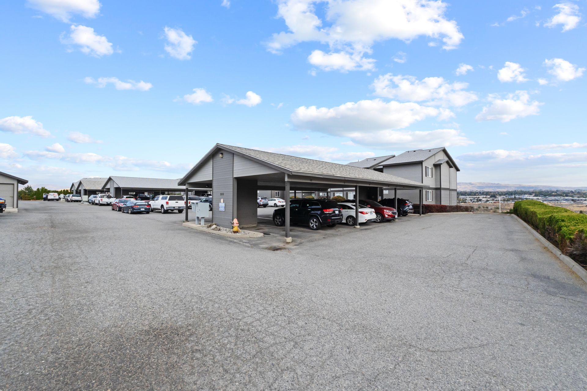 A parking lot with cars parked under a covered area in front of a building.