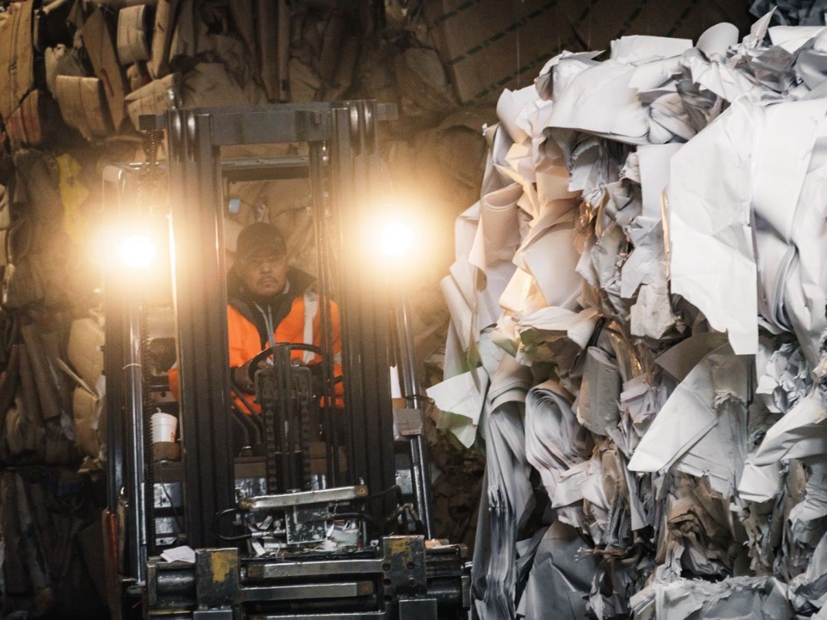 A Man Is Driving a Forklift in Front of A Pile of Paper.