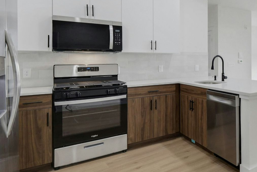 Modern kitchen with white upper cabinets, wood-tone lower cabinets, stainless steel appliances, and white countertops.